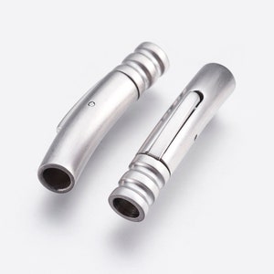 May include: Two silver metal bracelet clasps. One clasp is a straight tube with a sliding mechanism. The other clasp is a curved tube.