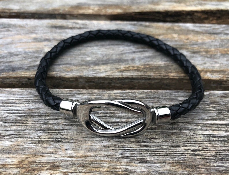 May include: A black leather bracelet with a silver knot clasp.