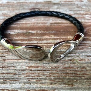 May include: A black leather bracelet with a silver clasp. The clasp is a hook and loop design.