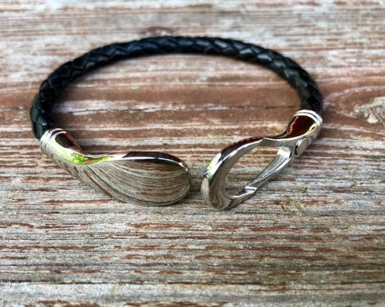 May include: A black leather bracelet with a silver clasp. The clasp is a hook and loop design.
