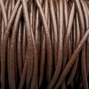 May include: Close-up of a spool of brown leather cord. The cord is tightly wound and has a smooth, polished finish.