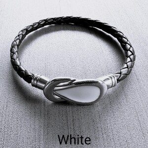 May include: A black leather bracelet with a white, ceramic hook clasp. The bracelet is braided and has a simple design.