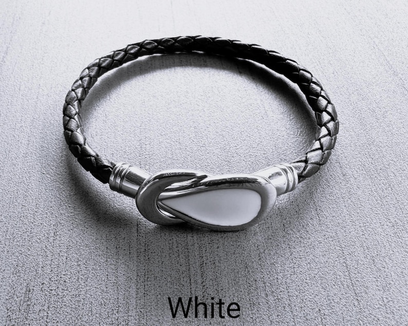 May include: A black leather bracelet with a white, ceramic hook clasp. The bracelet is braided and has a simple design.