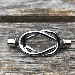 May include: A silver metal knot-shaped drawer pull. The pull is smooth and shiny.