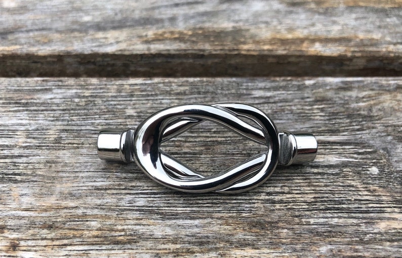 May include: A silver metal knot-shaped drawer pull. The pull is smooth and shiny.