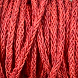 May include: Close-up of a red braided leather cord. The cord is made of multiple strands of leather that are woven together to create a thick, durable cord.