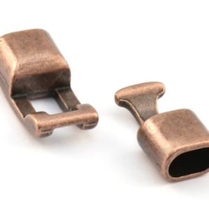 May include: Two antique copper-toned metal clasps for jewelry making. One clasp is a rectangular toggle with a small opening. The other clasp is a round barrel with a small opening.