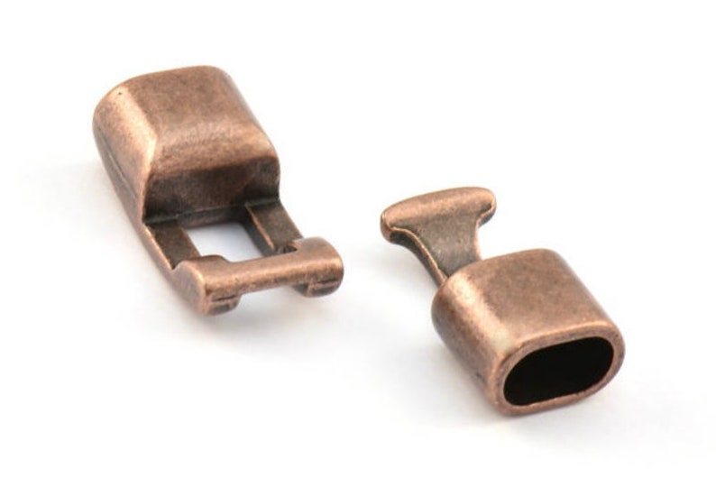 Peut inclure: Deux fermoirs m&eacute;talliques de couleur cuivre antique pour la fabrication de bijoux. Un fermoir est un bouton rectangulaire avec une petite ouverture. L'autre fermoir est un barillet rond avec une petite ouverture.