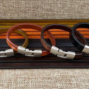 May include: Four leather bracelets with silver clasps. The bracelets are in brown, orange, green, and black.
