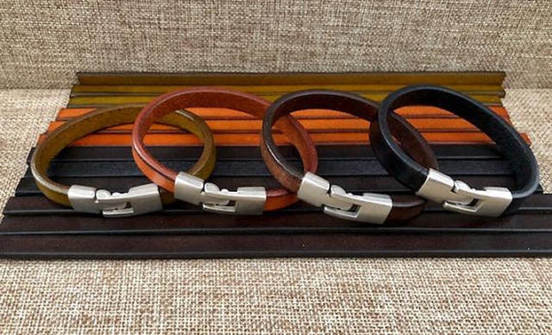 May include: Four leather bracelets with silver clasps. The bracelets are in brown, orange, green, and black.