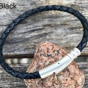 May include: Black leather bracelet with a silver magnetic clasp. The bracelet is braided and has a simple design.