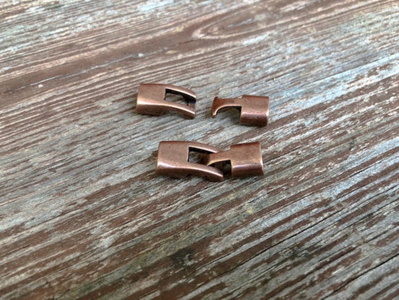 Peut inclure: Trois fermoirs m&eacute;talliques de couleur cuivre pour la fabrication de bijoux. Les fermoirs sont rectangulaires avec une petite ouverture d'un c&ocirc;t&eacute; et un crochet de l'autre.