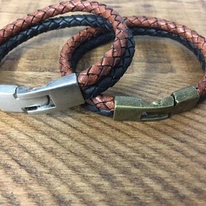 May include: Two leather bracelets with metal clasps. One bracelet is brown and black, the other is brown and tan.