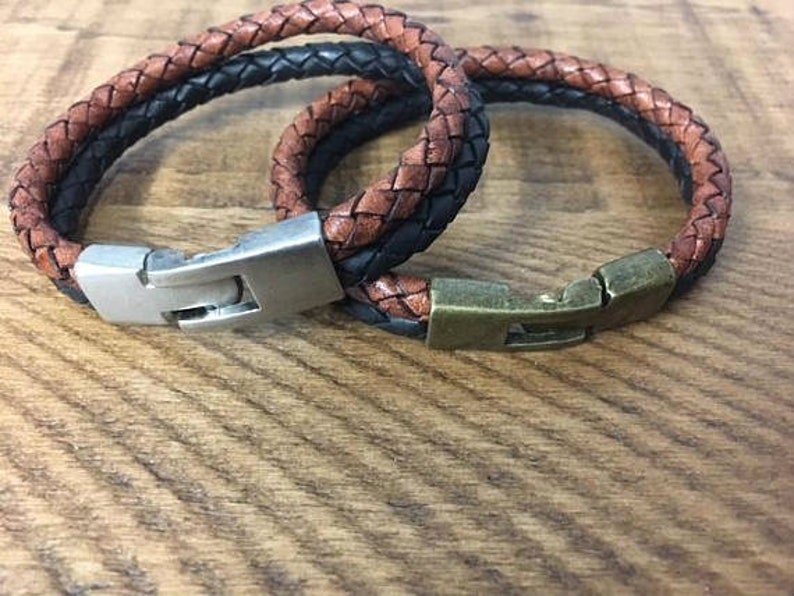 May include: Two leather bracelets with metal clasps. One bracelet is brown and black, the other is brown and tan.
