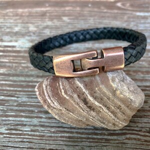 Peut inclure: Un bracelet en cuir tress&eacute; noir avec une fermeture en cuivre.
