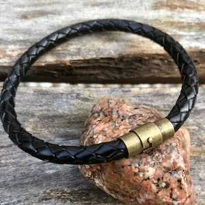 May include: A black leather bracelet with a braided design and a gold-toned magnetic clasp.