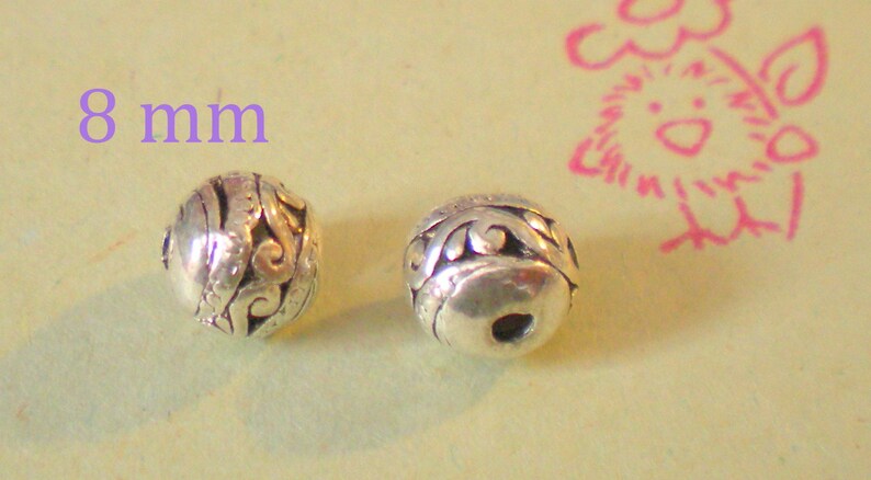 May include: Two silver beads with an intricate design, each measuring 8 mm in diameter.