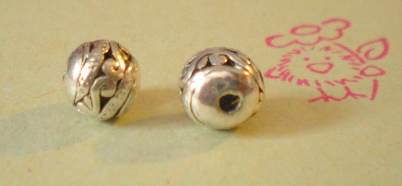 May include: Two silver beads with intricate designs. The beads are round and have a hole in the center.