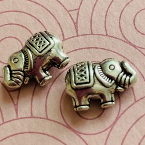 May include: Two silver elephant charms with intricate details. The elephants are facing to the right and have raised trunks.