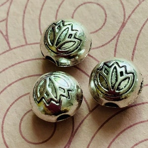 May include: Three silver metal beads with a lotus flower design. The beads have a hole through the center for stringing.
