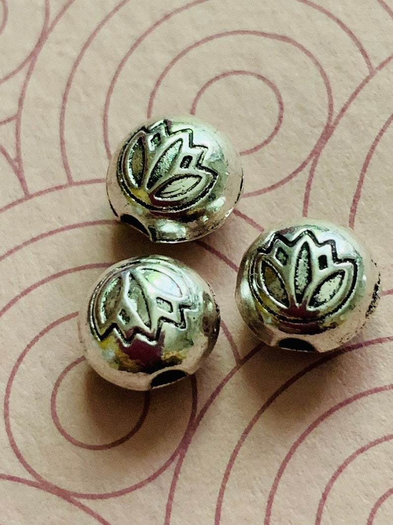 May include: Three silver metal beads with a lotus flower design. The beads have a hole through the center for stringing.