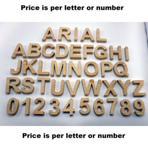 May include: Wooden letters and numbers in a light brown color are arranged on a white surface. The letters are in the Arial font. The numbers 0 through 9 are also displayed. The text "Price is per letter or number" is above and below the letters and numbers.