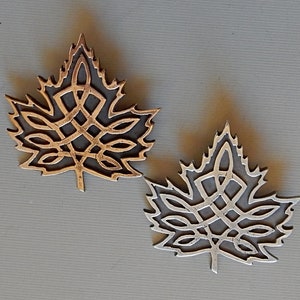 May include: Two metal maple leaf pendants featuring intricate Celtic knot designs. One pendant is gold and the other is silver.