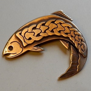 May include: A gold-coloured metal fish pendant featuring a Celtic knot design. The fish is depicted leaping with its tail curled around its body.