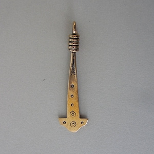 Könnte beinhalten: Ein goldfarbener Metallanhänger in Form eines Hammers mit einer Schlaufe oben. Der Hammer hat ein dekoratives Design aus Kreisen und Punkten.