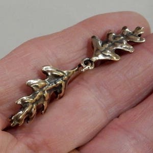 May include: A gold-toned metal oak leaf charm with a textured surface. The charm is designed to be a pendant or a decorative element for jewellery.
