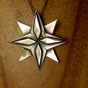 Eight point bronze star. Four triangular points are on the lowest layer.  Four more points overlay these filling in between them.  The top four points have a raised elongated diamond shape on top of them.  On chain. By Master Ark.