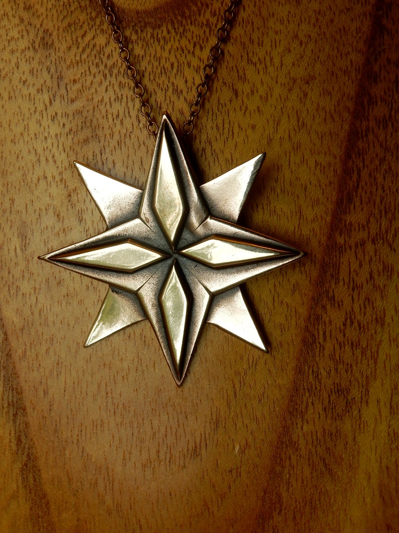 Eight point bronze star. Four triangular points are on the lowest layer.  Four more points overlay these filling in between them.  The top four points have a raised elongated diamond shape on top of them.  On chain. By Master Ark.