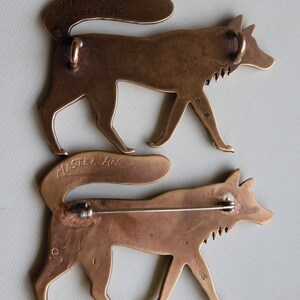 Back of Master Ark's wolf showing two wolves, one with a pin back and the other with two suspension loops for hanging as a pendant.