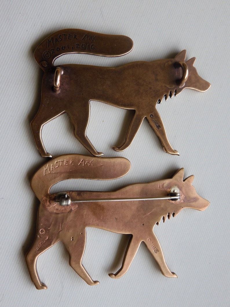 Back of Master Ark's wolf showing two wolves, one with a pin back and the other with two suspension loops for hanging as a pendant.