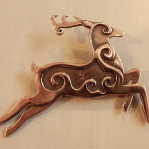 Right facing leaping stag decorated with Celtic style spirals on body and face.  Two layers of metal so the spiral patterns are raised. Hind legs extended, front legs folded downward, tail erect, head upright.  Cast bronze by Master Ark.