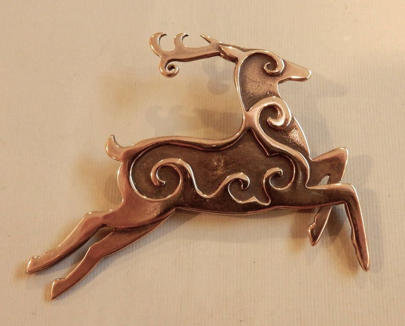 Right facing leaping stag decorated with Celtic style spirals on body and face.  Two layers of metal so the spiral patterns are raised. Hind legs extended, front legs folded downward, tail erect, head upright.  Cast bronze by Master Ark.