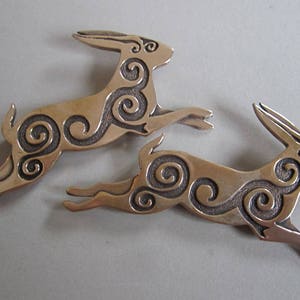 Two running rabbits pictured with one jumping above the other.  Rabbits are in profile, facing right.  Decorated with Celtic spirals cut into the body.  Bronze by Master Ark.