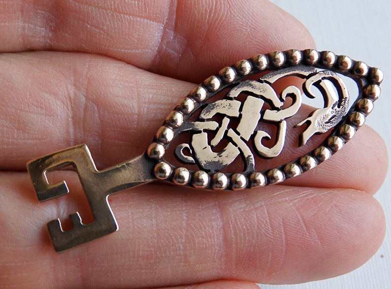 May include: A gold-toned key with a detailed Celtic knot design and a beaded border. The key has a simple, straight handle.