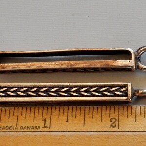 Side and front view of bronze bars to slide onto a belt with a suspension loop at the bottom.  Herringbone wire pattern on the front in a boxed border.  By Master Ark.
