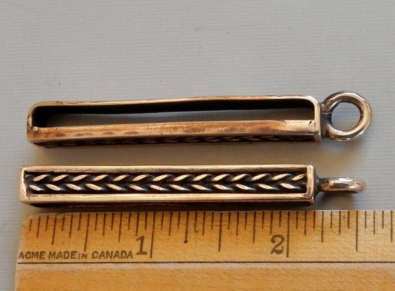 Side and front view of bronze bars to slide onto a belt with a suspension loop at the bottom.  Herringbone wire pattern on the front in a boxed border.  By Master Ark.