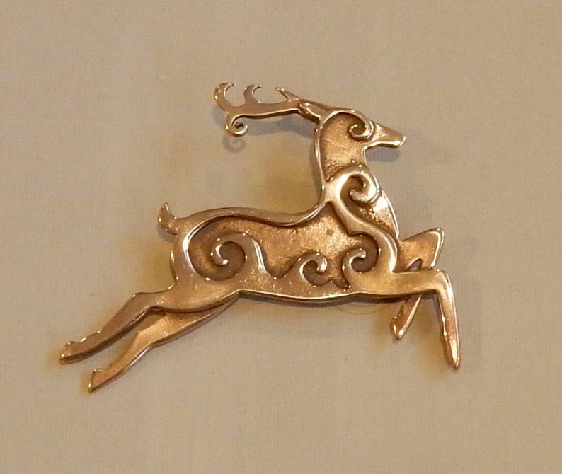 Right facing leaping stag decorated with Celtic style spirals on body and face.  Two layers of metal so the spiral patterns are raised. Hind legs extended, front legs folded downward, tail erect, head upright.  Cast bronze by Master Ark.