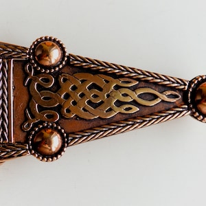 May include: A triangular copper belt buckle with a Celtic knot design and three round copper accents.