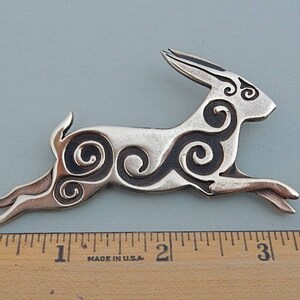 Running rabbit in profile, facing right.  Decorated with Celtic spirals cut into the body.  Pictured with ruler - 3 1/4 inches long. 
 Bronze by Master Ark.