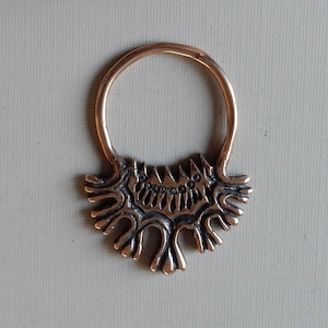 Op de afbeelding: Een bronzen ring met een decoratief ontwerp met een gestileerde boom met een reeks kleine cirkels op de takken.