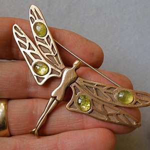 May include: A bronze dragonfly brooch with four yellow glass cabochons set into the wings. The brooch is attached to a pin.