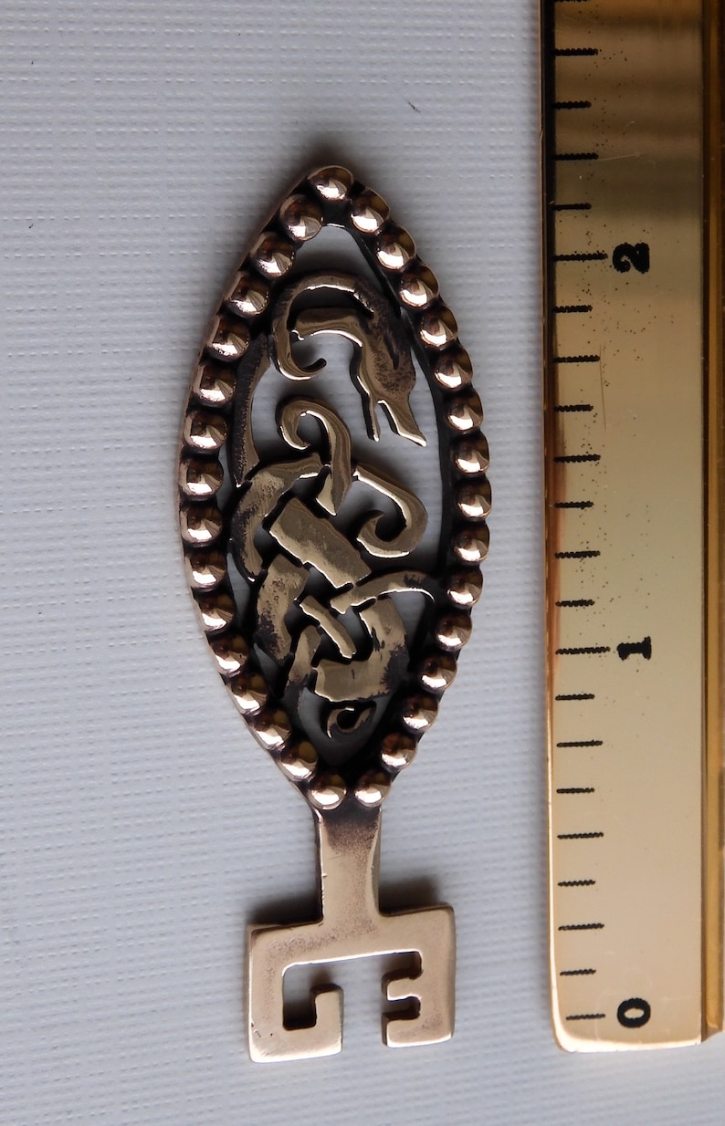 May include: A bronze key with an ornate design featuring a stylized knotwork pattern. The key has a rounded oval head and a square-shaped bow.