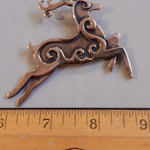 Right facing leaping stag decorated with Celtic style spirals on body and face.  Two layers of metal so the spiral patterns are raised. Hind legs extended, front legs folded downward, tail erect, head upright. Shown next to ruler - 3 inches.