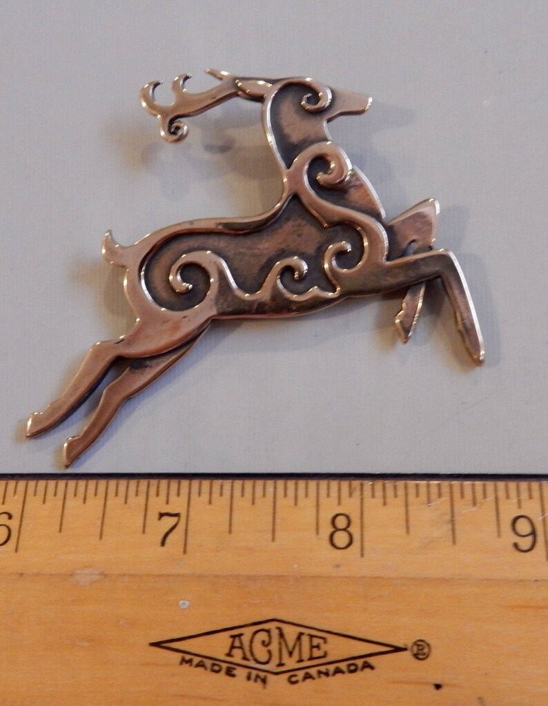 Right facing leaping stag decorated with Celtic style spirals on body and face.  Two layers of metal so the spiral patterns are raised. Hind legs extended, front legs folded downward, tail erect, head upright. Shown next to ruler - 3 inches.