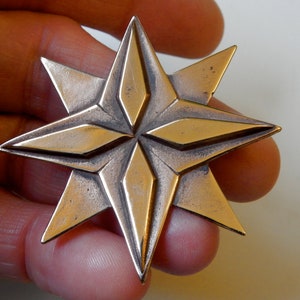 Eight point bronze star. Four triangular points are on the lowest layer.  Four more points overlay these filling in between them.  The top four points have a raised elongated diamond shape on top of them.  Pictured in hand. By Master Ark.