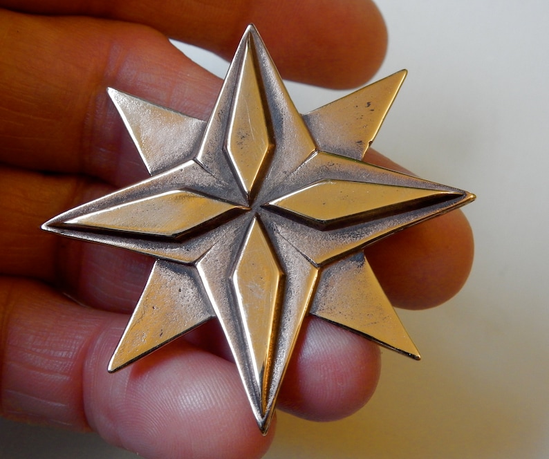 Eight point bronze star. Four triangular points are on the lowest layer.  Four more points overlay these filling in between them.  The top four points have a raised elongated diamond shape on top of them.  Pictured in hand. By Master Ark.